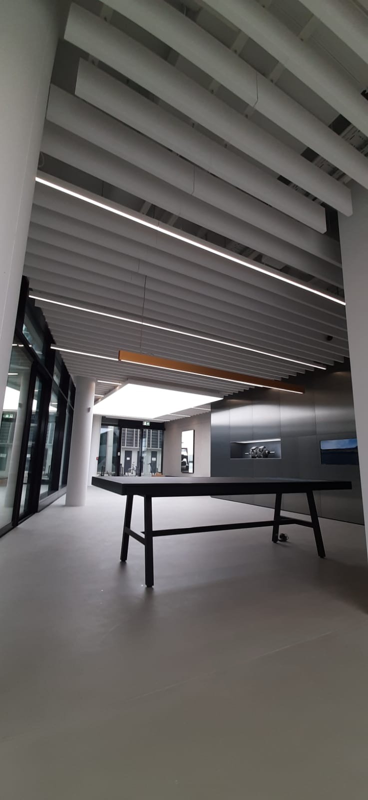 Nowoczesne wnętrze biurowe z podwieszanym sufitem i oświetleniem LED. Minimalistyczny design z czarnym stołem konferencyjnym na pierwszym planie.