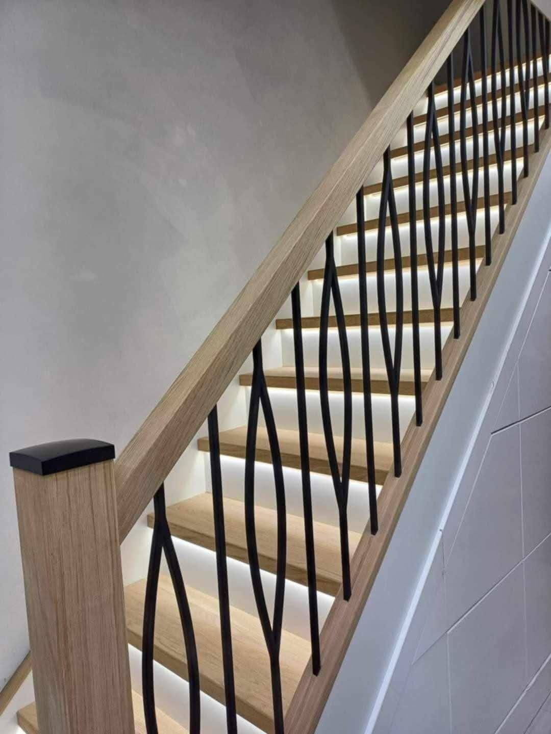 Nowoczesne schody z drewnianymi stopniami, podświetleniem LED i czarną, dekoracyjną balustradą. Jasne drewno i minimalistyczny design. Ujęcie z dołu.