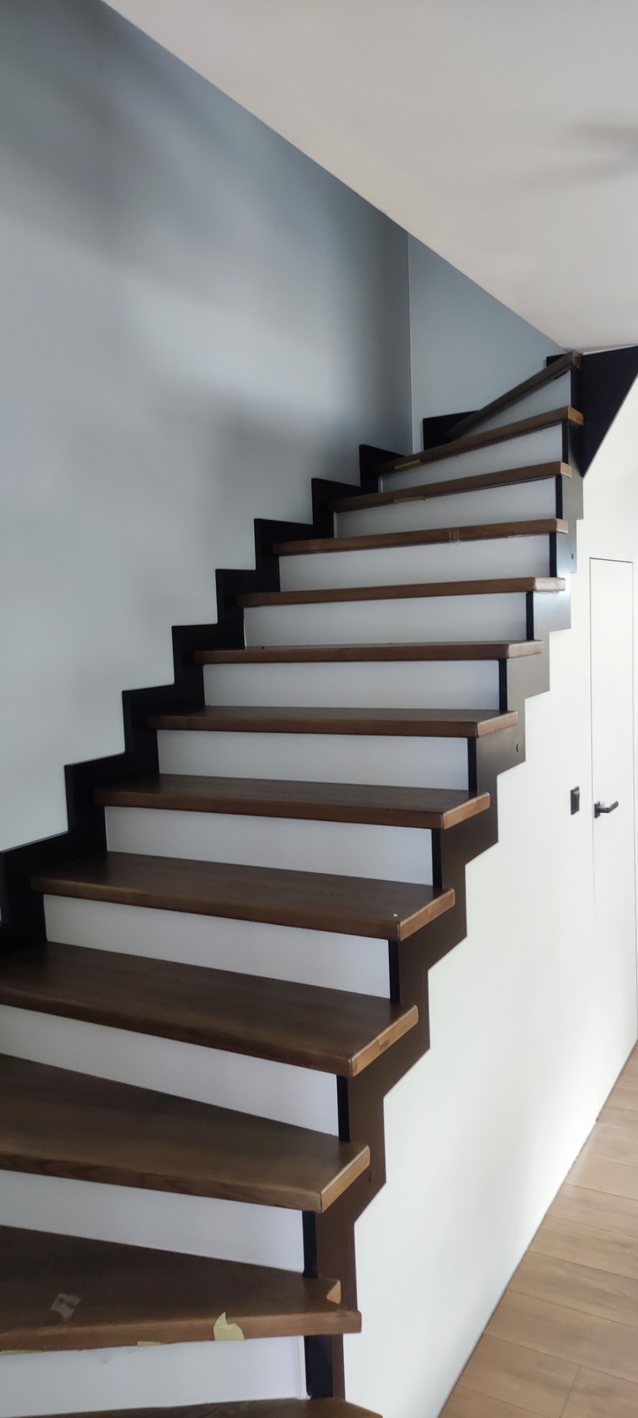 Drewniane schody z czarną metalową konstrukcją w Dębnie. Stopnie w odcieniach brązu, białe podstopnice. Nowoczesny design, minimalistyczne wykończenie.