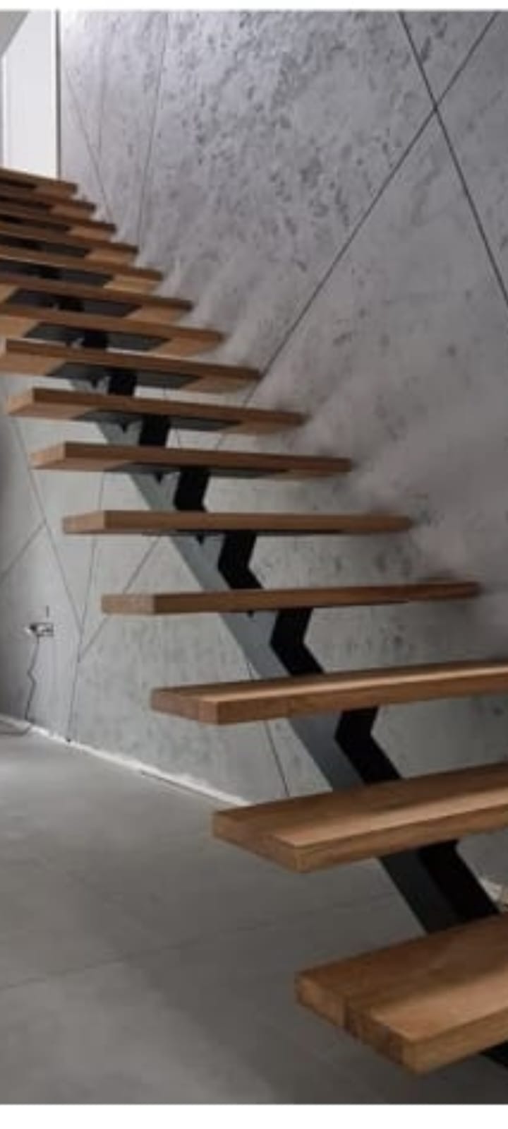 Nowoczesne schody z drewnianymi stopniami i czarną, metalową konstrukcją na tle betonowej ściany z geometrycznym wzorem. Minimalistyczny design.