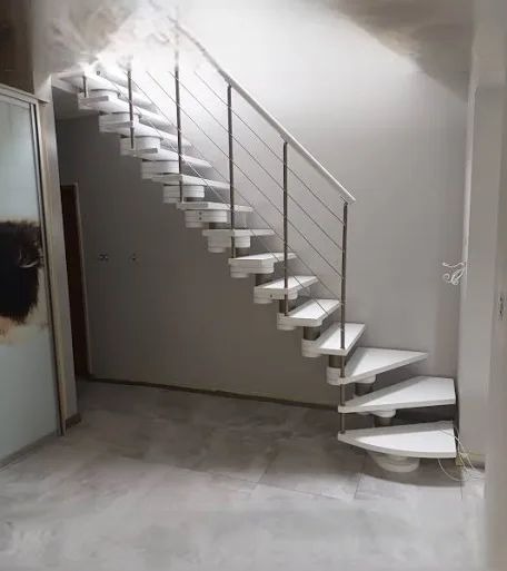 Białe schody spiralne z metalową balustradą w jasnym wnętrzu. Nietypowy kształt stopni, minimalistyczny design, widok z dołu. Nowoczesne schody w wykończonym domu.
