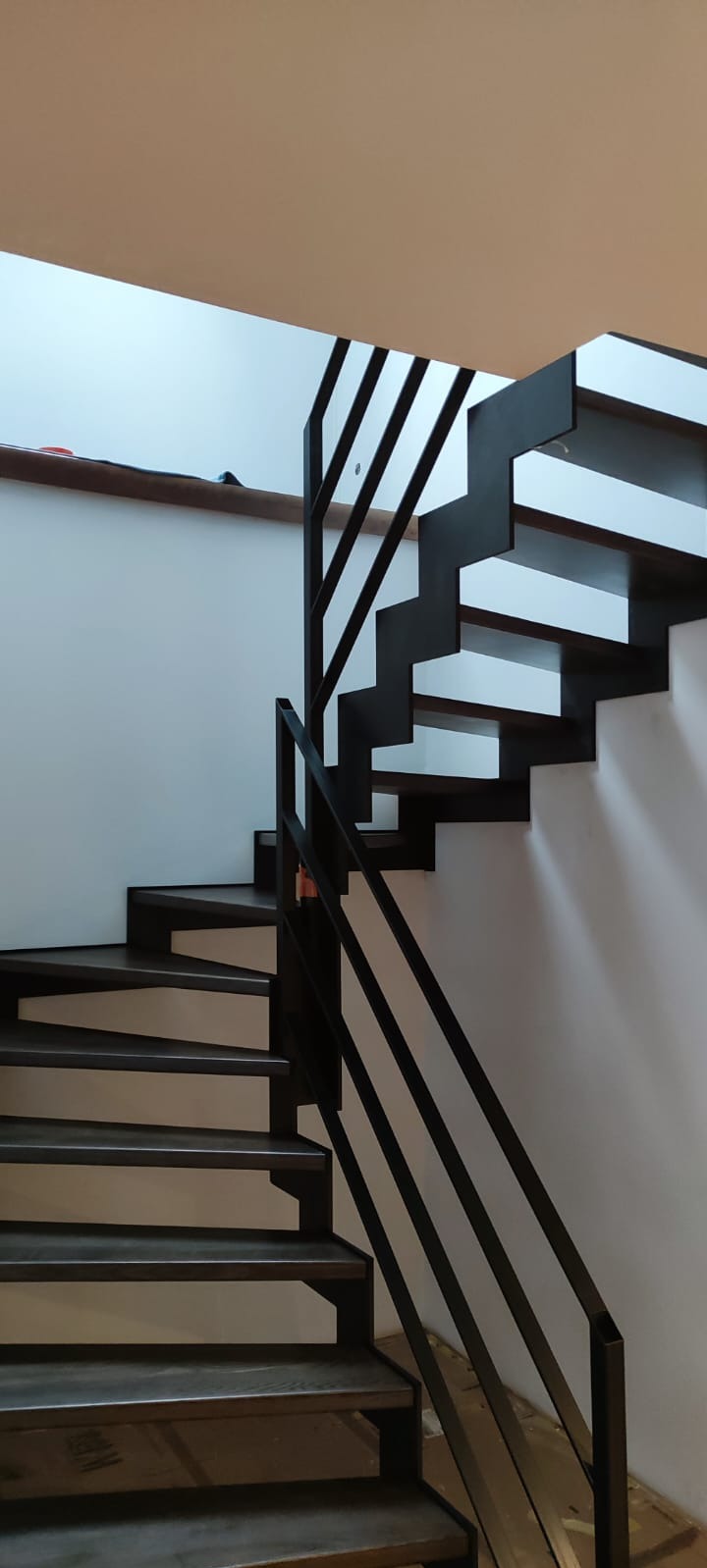 Nowoczesne schody z drewnianymi stopniami i czarną, minimalistyczną balustradą. Ujęcie z dołu, podkreślające geometrię konstrukcji i kontrast bieli ścian.