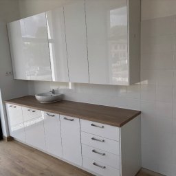 Tomasz Michalski - Białe, lakierowane szafki łazienkowe z drewnianym blatem i okrągłą umywalką, z widocznym oknem po lewej stronie i białymi kafelkami na ścianie.