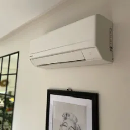 Biała klimatyzacja Panasonic zamontowana na ścianie w Grodzisku Mazowieckim. Pod spodem czarno-biała fotografia w ramie. Widoczne elementy dekoracyjne.