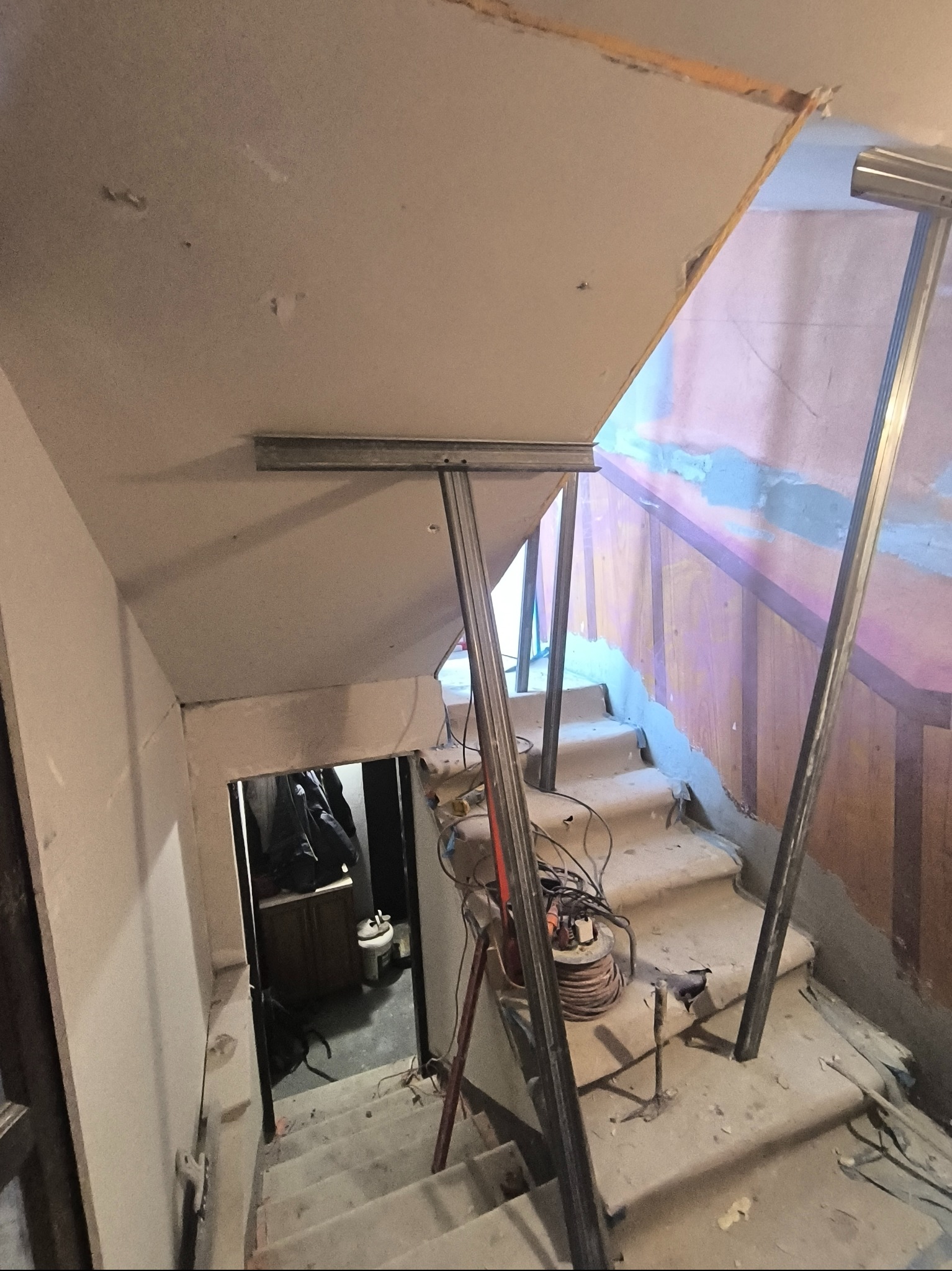 Montaż stelażu pod płytę G-K na schodach. Widoczne profile, przewody i narzędzia. Etap prac wykończeniowych wewnątrz budynku. Ujęcie z dołu schodów.