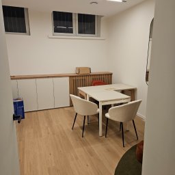 Michał partyga - Jasne biuro z drewnianą podłogą, białymi ścianami i meblami. Widoczne biurko, krzesła i szafki w zabudowie. Minimalistyczny design z oświetleniem LED.