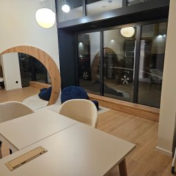 Michał partyga - Nowoczesne biuro z drewnianym lustrem w kształcie łuku, beżowymi krzesłami i stołem. Za oknem widoczny parking. Minimalistyczny design wnętrza.