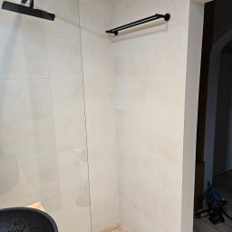 Michał partyga - Wykończona łazienka w Radomiu: jasne płytki, drewnopodobna podłoga, czarna armatura i szklana kabina prysznicowa. Minimalistyczny design.