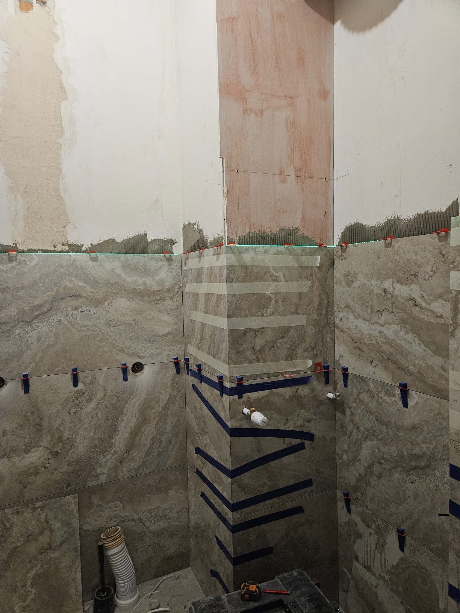 Układanie płytek imitujących marmur w łazience w Radomiu. Widoczne poziomice laserowe i system poziomowania płytek. Częściowo wykończone ściany.
