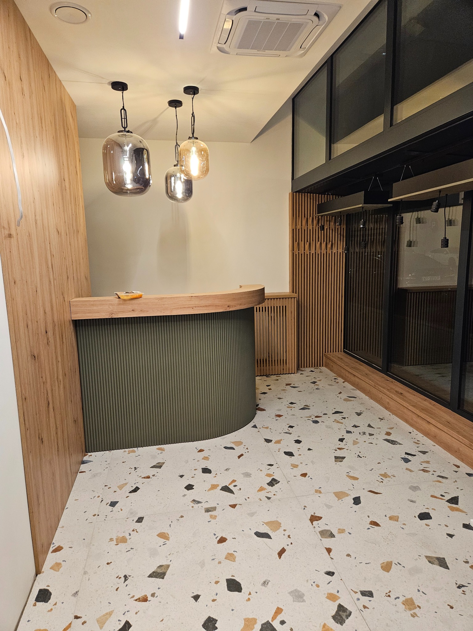 Nowoczesne wnętrze w Radomiu z recepcją o zaokrąglonym froncie, drewnianymi panelami i designerskimi lampami wiszącymi. Podłoga wyłożona płytkami lastryko.