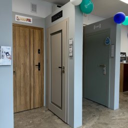 Vizera Sp. z o.o. - Ekspozycja trzech modeli drzwi wewnętrznych różnych producentów (Doorpol, Berkado, Porta) w salonie, z balonami reklamowymi pod sufitem i katalogami na ścianie.