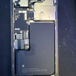 Wnętrze rozłożonego iPhone'a z widoczną baterią, płytą główną i innymi komponentami. Ukazany etap demontażu w serwisie telefonów. Widoczny napis 'TAPTIC ENGINE'.