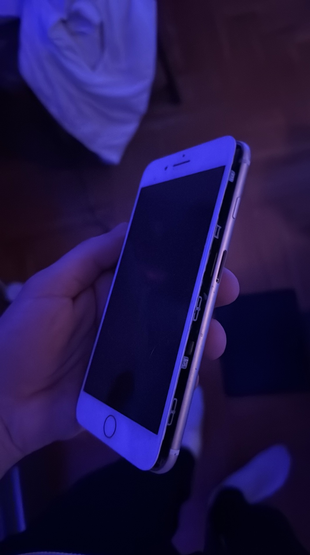 Rozłożony iPhone w dłoni, widoczne wnętrze obudowy. Smartfon w trakcie naprawy/serwisu, podświetlony niebieskim światłem. Nietypowe ujęcie stanu urządzenia.