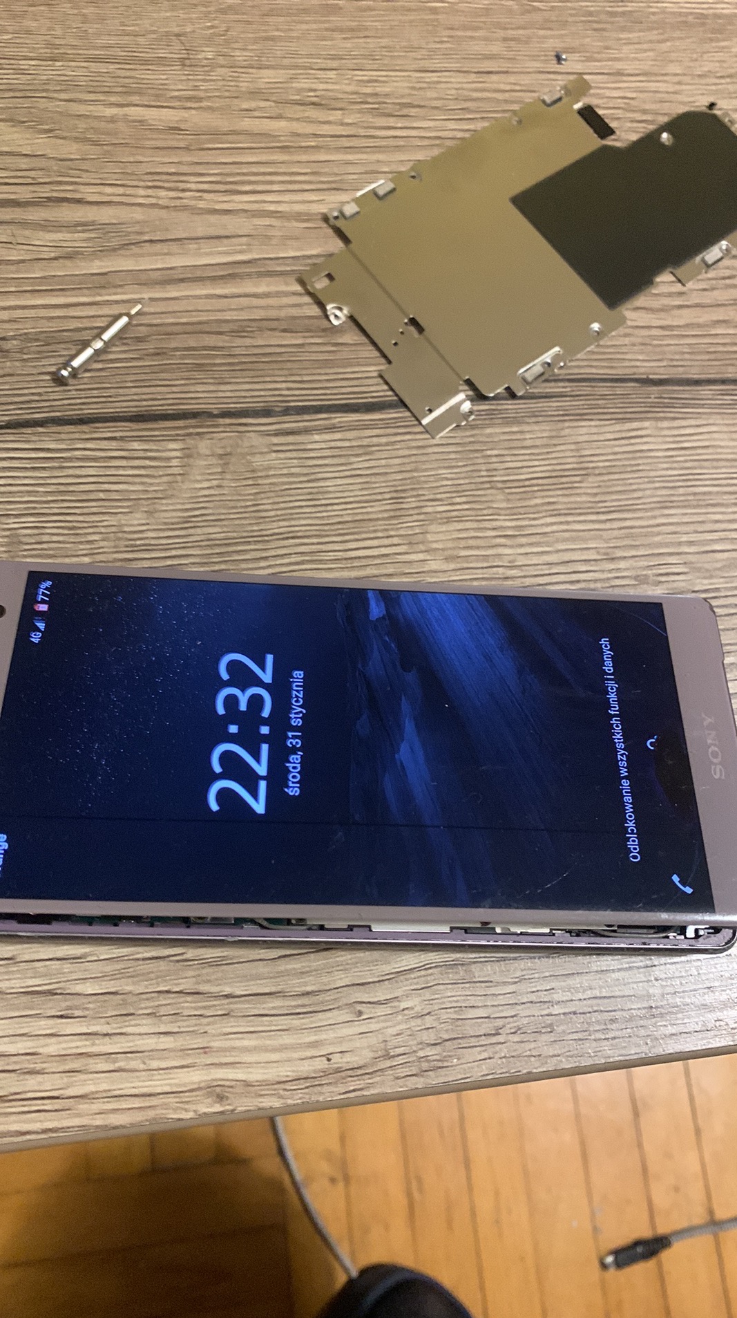 Rozłożony smartfon Sony Xperia na drewnianym stole, obok narzędzia serwisowe i metalowa obudowa. Ekran wyświetla godzinę 22:32.