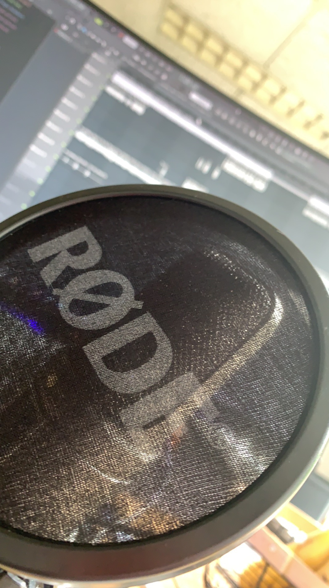 Pop filtr mikrofonu RØDE z widocznym ekranem komputera w tle, prezentujący oprogramowanie do produkcji muzyki. Ujęcie z bliska, podkreślające detale siatki filtra.