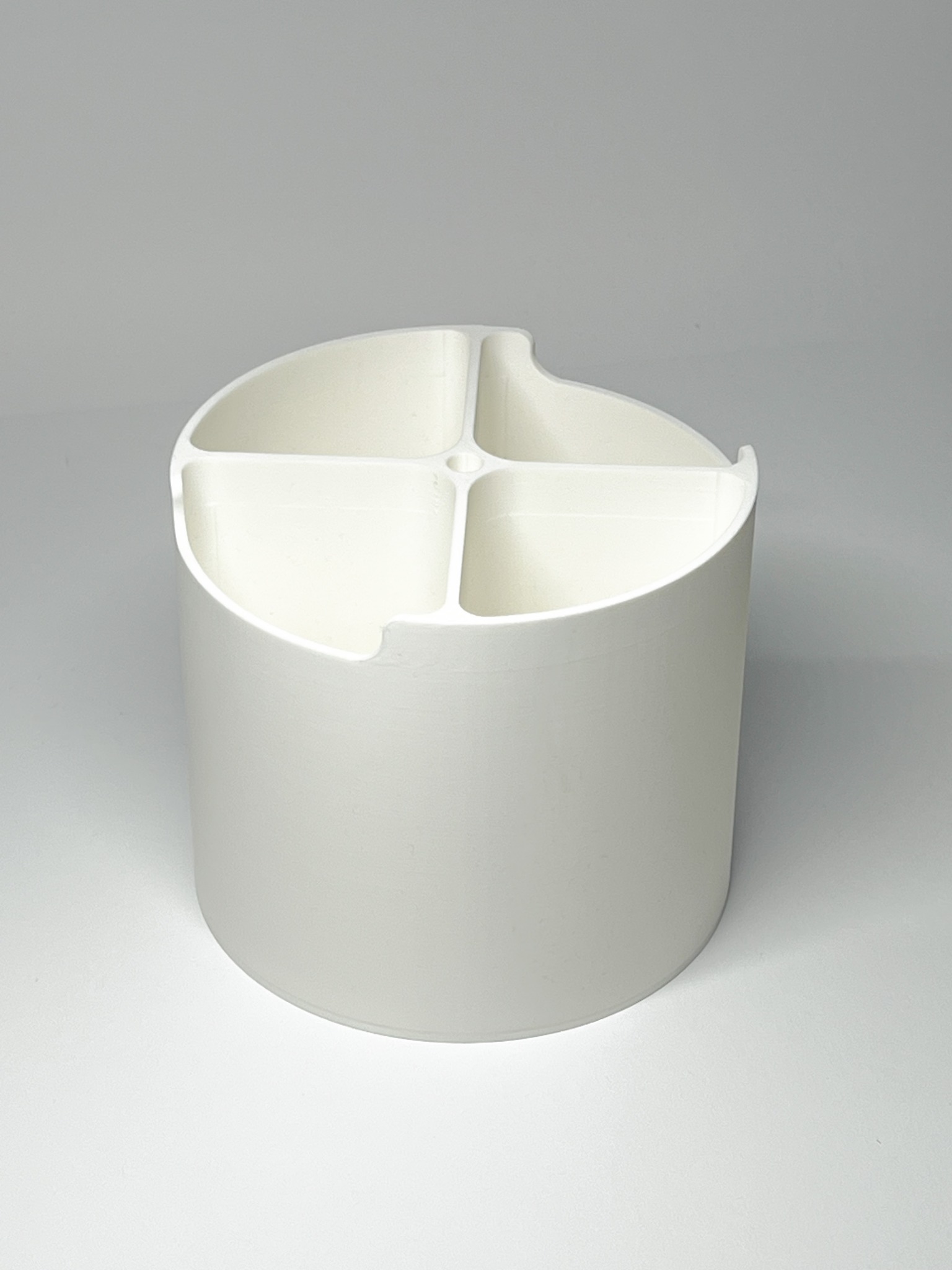 Biały, cylindryczny organizer z przegródkami, wydrukowany w 3D. Widoczne charakterystyczne warstwy druku. Stojący pionowo na jasnym tle.