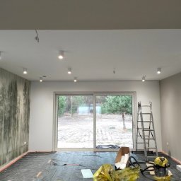 MONTE KABLO USŁUGI ELEKTRYCZNE DOMINIK KAPTUR - Wnętrze pokoju z zamontowanym oświetleniem sufitowym typu spot. Widoczne przewody do podłączenia lamp, drabina, okno tarasowe i podłoga zabezpieczona folią.
