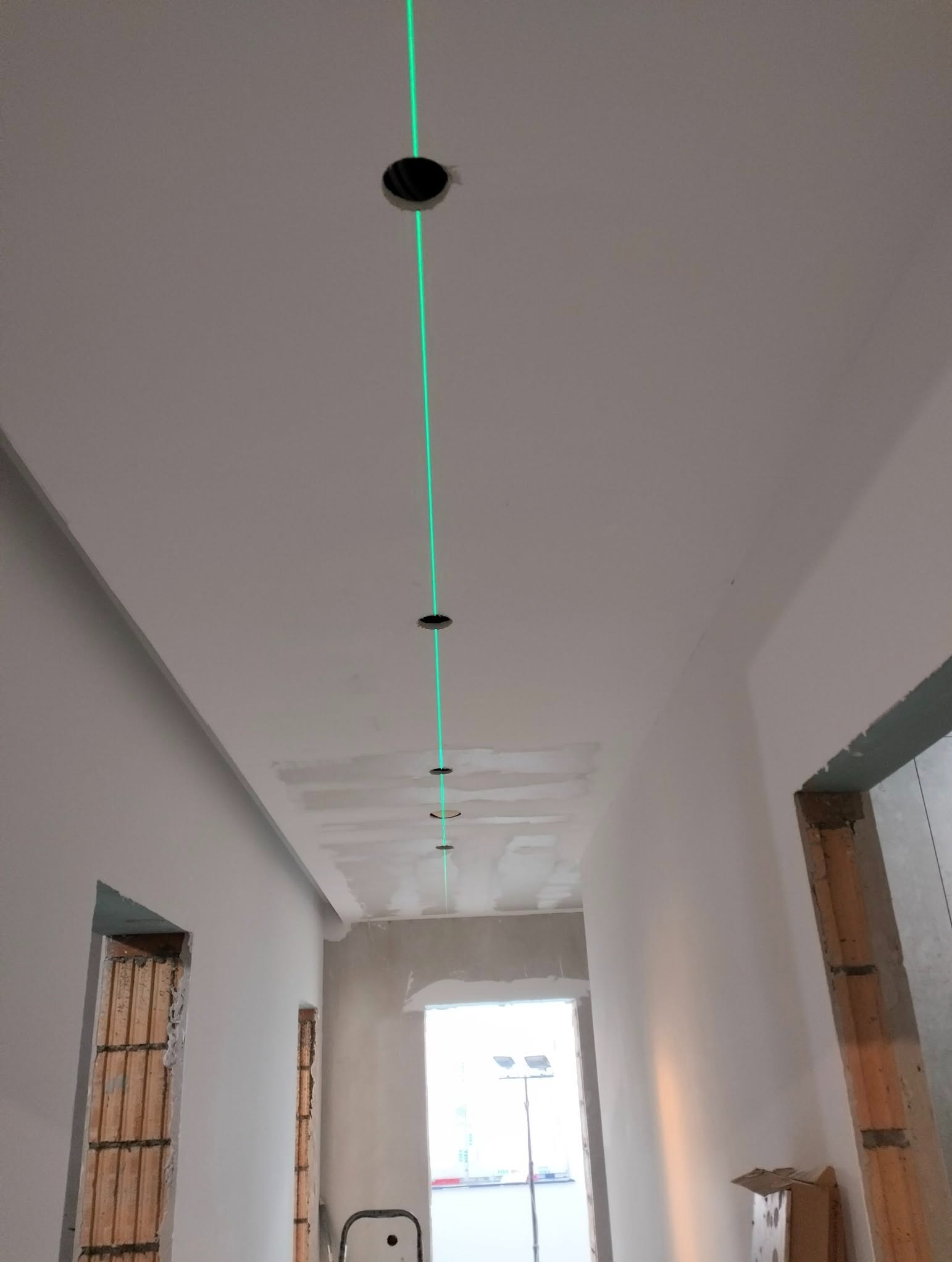 Wyrównywanie otworów w suficie pod montaż oświetlenia za pomocą lasera krzyżowego. Widoczne otwory w równej linii. Ściany w trakcie wykończenia.