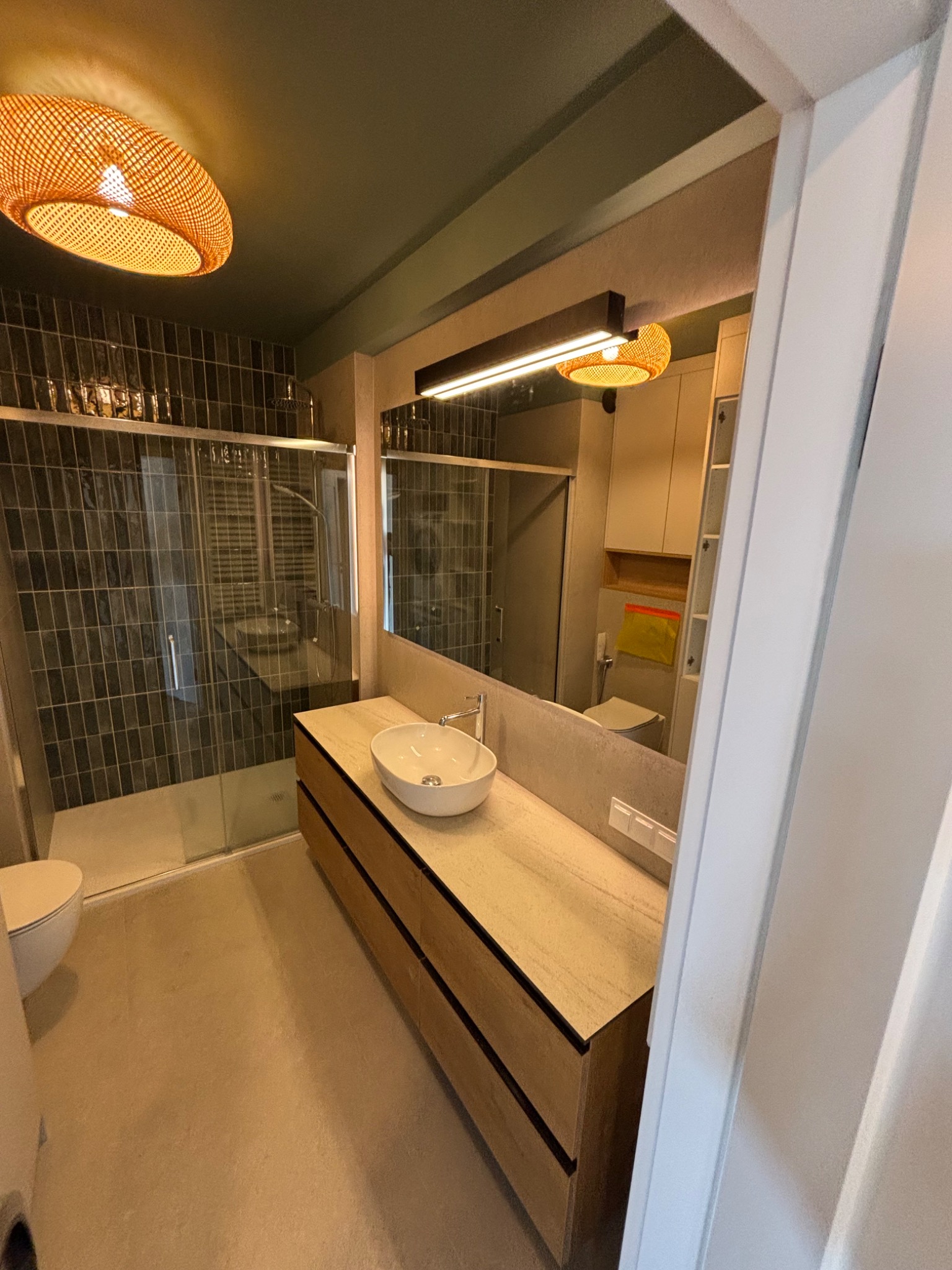 Nowoczesna łazienka w Iławie z kabiną prysznicową, umywalką nablatową i drewnianą szafką pod umywalką. W tle widoczne płytki w odcieniach szarości i oświetlenie.