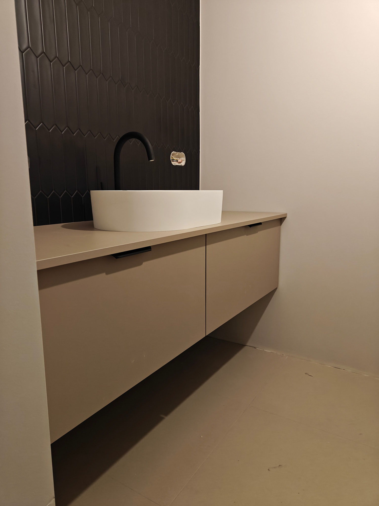 Nowoczesna łazienka: beżowa szafka z umywalką nablatową i czarną armaturą na tle ściany z ciemnych, podłużnych płytek. Minimalistyczny design.