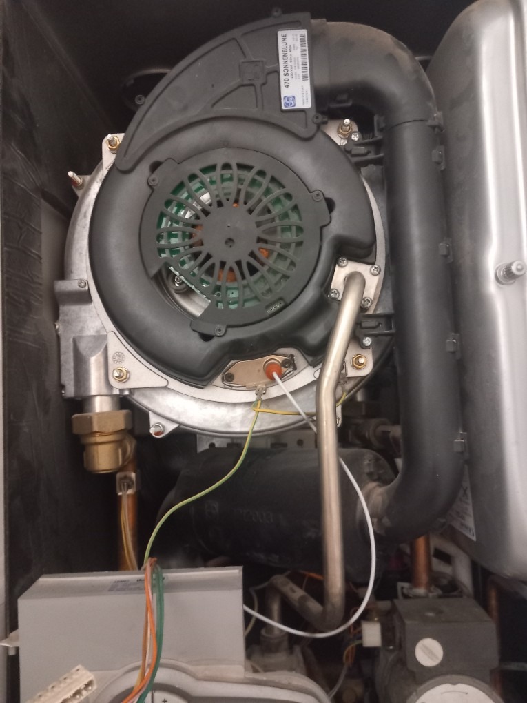 Wnętrze kotła gazowego z widocznym wentylatorem i przewodami. Detaliczny widok na elementy instalacji grzewczej, prezentujący skomplikowaną budowę urządzenia.