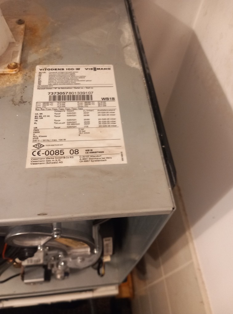 Szczegółowe ujęcie tabliczki znamionowej pieca gazowego Viessmann Vitodens 100-W z widocznym numerem seryjnym i parametrami technicznymi, umieszczonego przy ścianie.