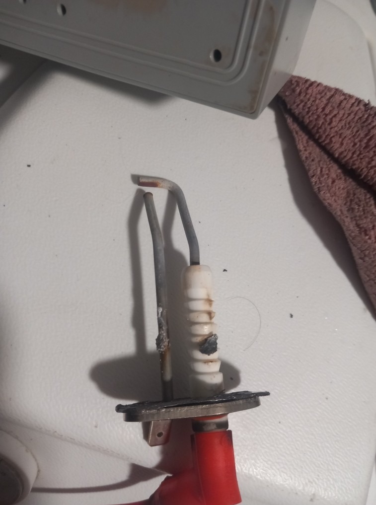 Uszkodzona elektroda jonizacyjna pieca gazowego z widocznymi śladami przepalenia, z bliska. Element zdemontowany, przygotowany do wymiany podczas serwisu.