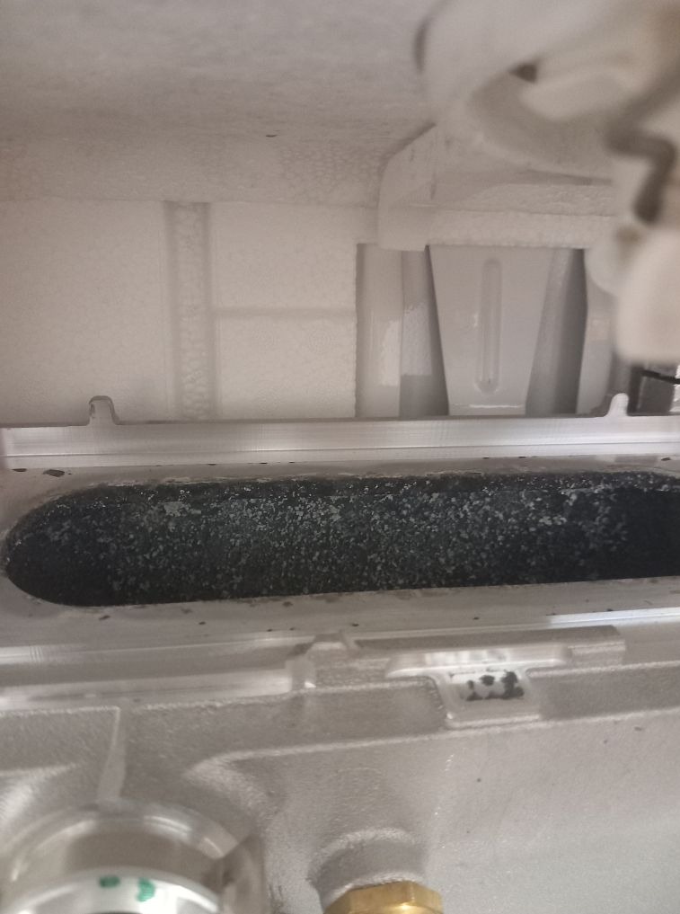 Wnętrze pieca gazowego z widocznym palnikiem i elementami izolacyjnymi. Palnik pokryty osadem, sugerujący potrzebę serwisu.