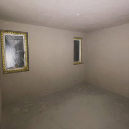 ZIAJBUD - Wnętrze pokoju po szpachlowaniu ścian i sufitu, okna zabezpieczone folią i taśmą malarską, przygotowane do malowania. Minimalistyczny styl.