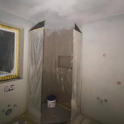 ZIAJBUD - Łazienka w trakcie remontu: obudowany prysznic folią ochronną, widoczne przygotowania do dalszych prac wykończeniowych, ślady po instalacjach.