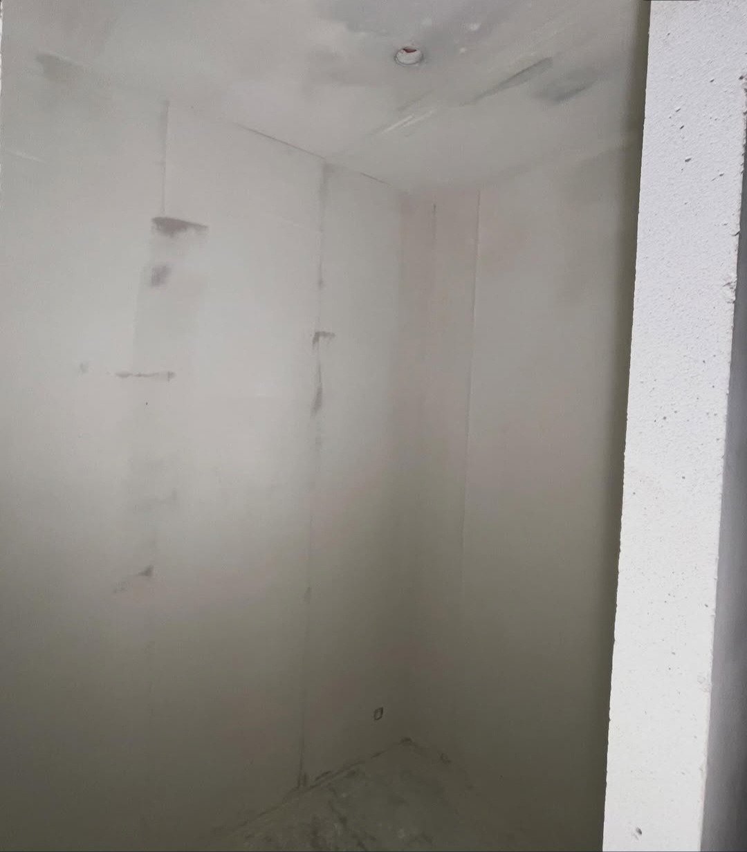 Wnętrze w trakcie szpachlowania: surowe ściany z widocznymi śladami szpachli, przygotowywane do dalszych prac wykończeniowych. Widoczny fragment sufitu i narożnik.