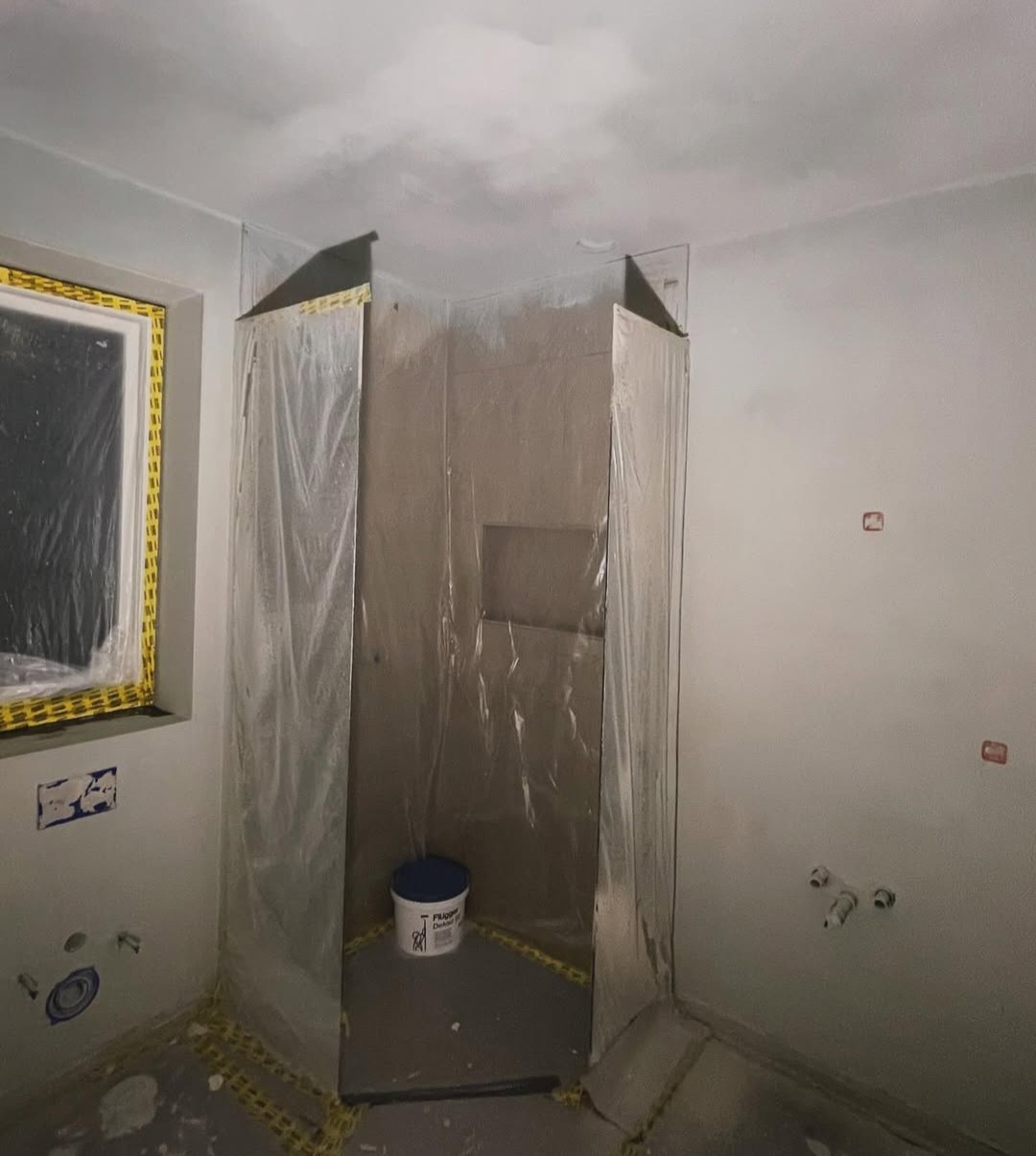 Łazienka w trakcie remontu: obudowany prysznic folią ochronną, widoczne przygotowania do dalszych prac wykończeniowych, ślady po instalacjach.