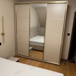 Damian Piekarski - Beżowa szafa przesuwna z lustrem w sypialni, widoczny fragment łóżka i lampka nocna. Na podłodze leżą narzędzia.