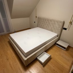 Damian Piekarski - Beżowe łóżko z tapicerowanym zagłówkiem w geometryczne wzory, wysunięta szuflada, drewniana podłoga. Nowoczesny design w sypialni na poddaszu.