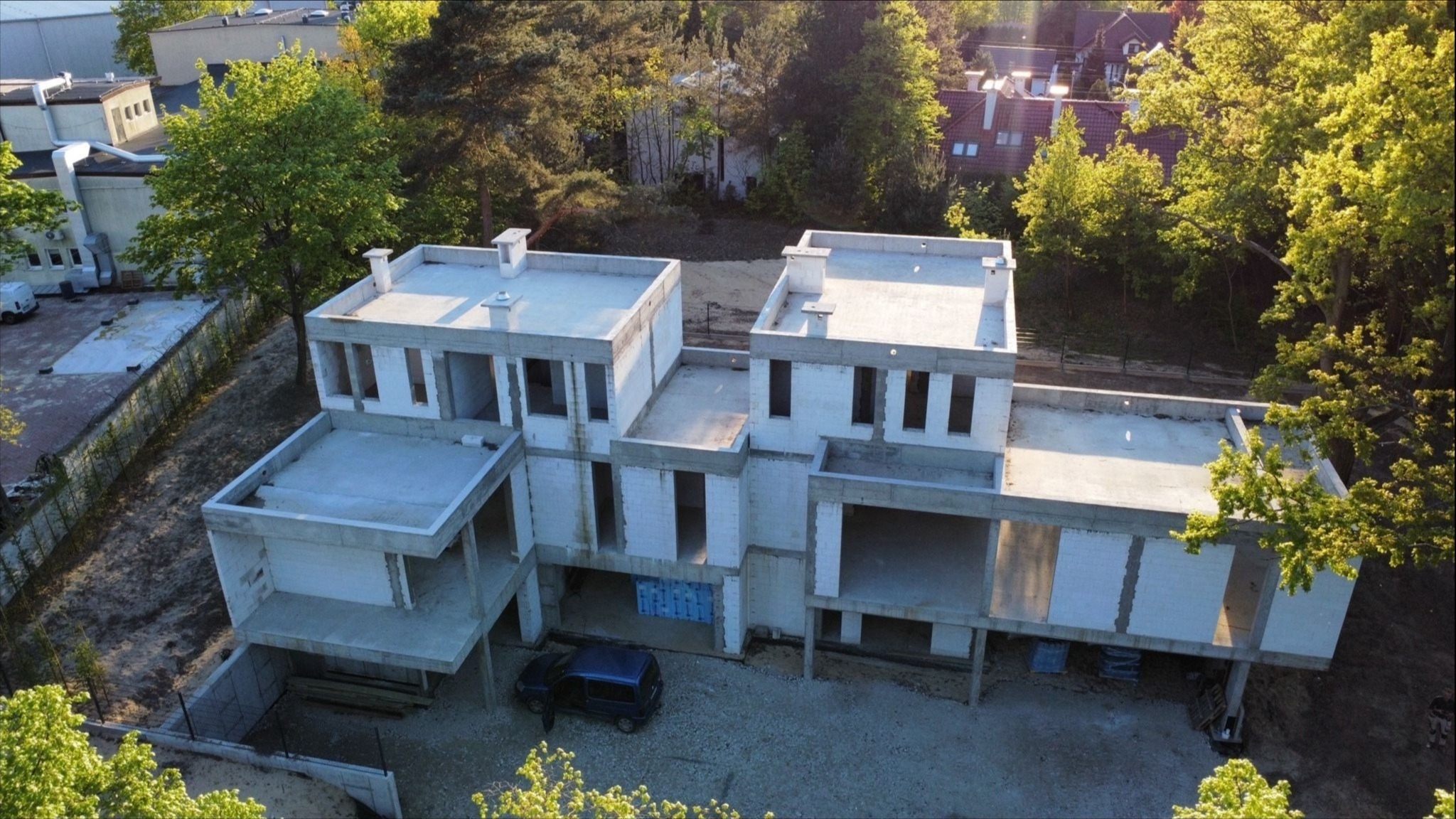 Surowy stan dwukondygnacyjnego, nowoczesnego domu z białego bloczka, widzianego z góry, z niebieskim vanem zaparkowanym obok na żwirowym podłożu.