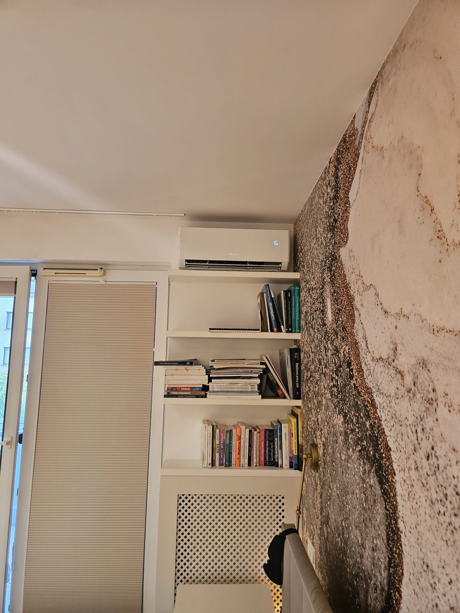 Biała klimatyzacja na ścianie w pokoju z półkami na książki, widok z dołu. Dekoracyjna tapeta na ścianie.