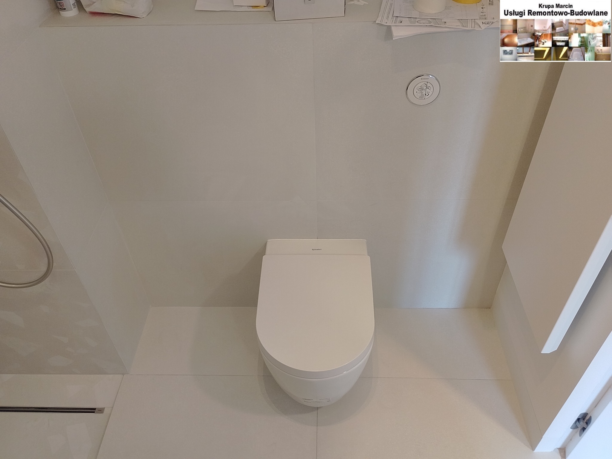 Nowoczesna toaleta wisząca Duravit w minimalistycznej łazience, wykończonej jasnymi płytkami. Widoczny panel sterujący i elementy armatury. Czyste, symetryczne ujęcie.