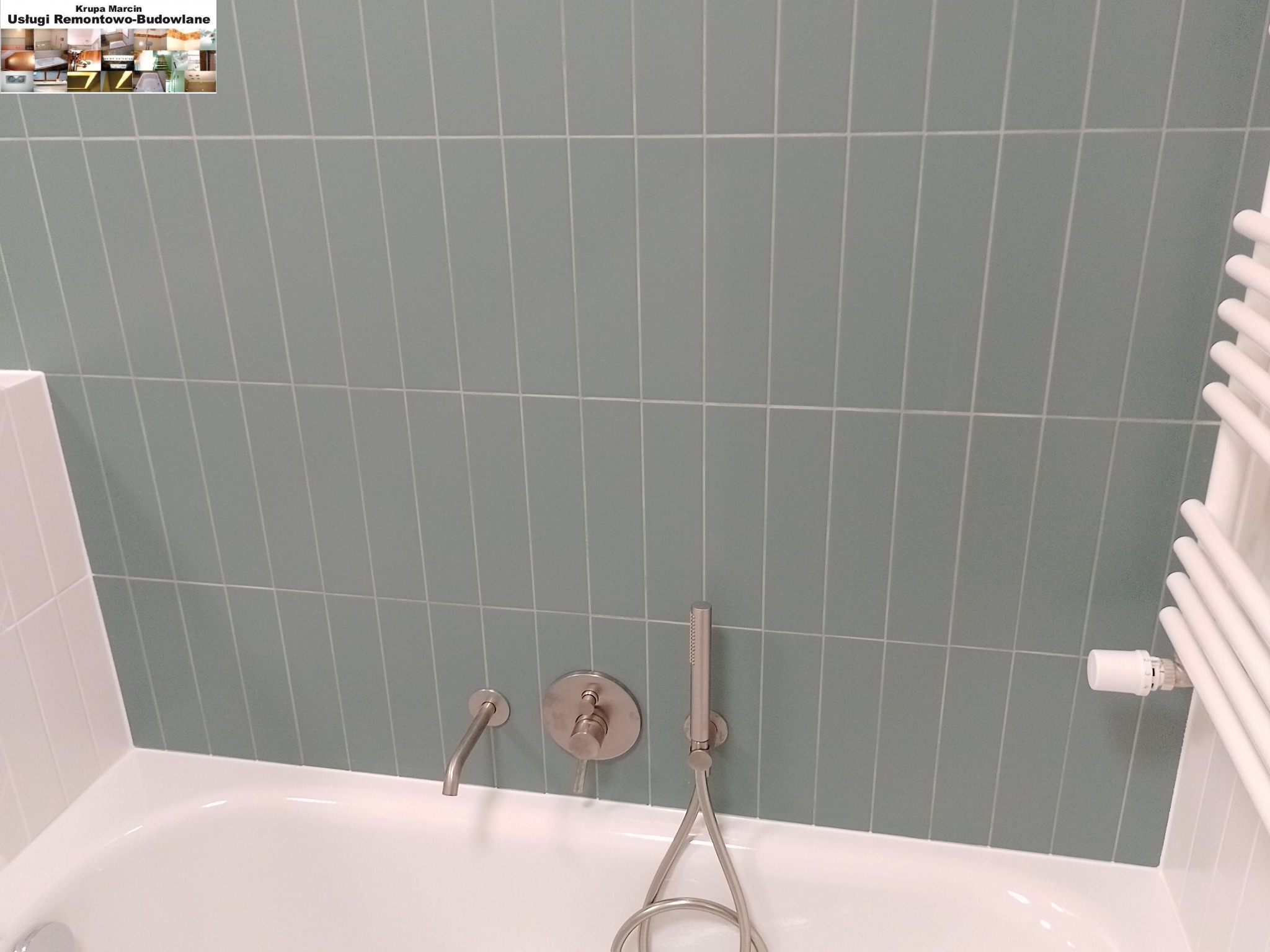 Błękitne, pionowe płytki w łazience nad białą wanną. Chromowana bateria i grzejnik drabinkowy po prawej. Minimalistyczny design.