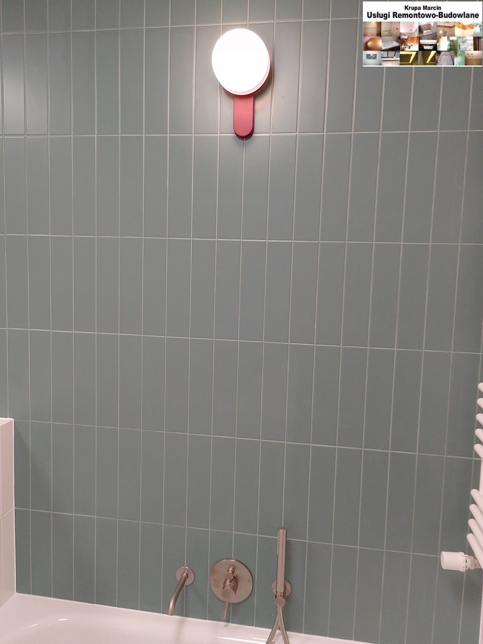 Wykończona ściana łazienki z pionowymi, smukłymi, szarymi płytkami, oświetlona okrągłą lampą. Widoczna bateria wannowa i grzejnik.