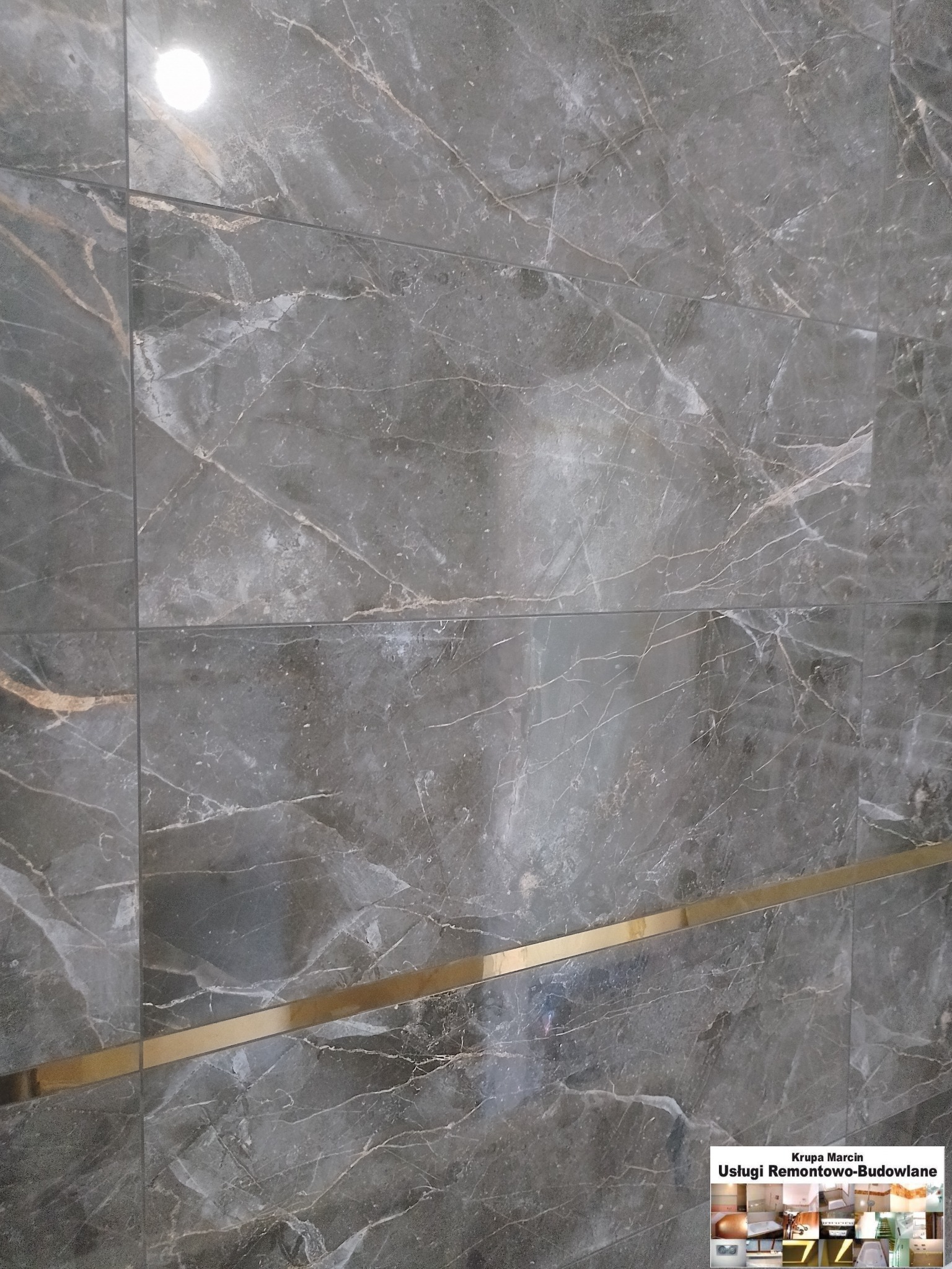 Eleganckie, szare płytki imitujące marmur z złotym akcentem, ułożone na ścianie. Widoczny fragment logo firmy remontowej w rogu.