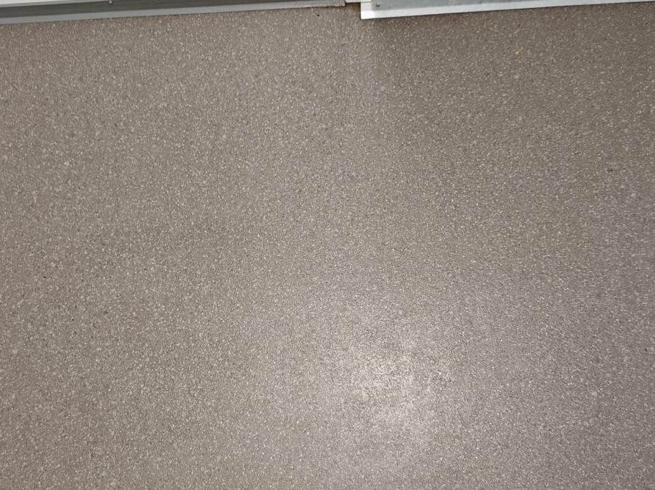 Szara, czysta posadzka z drobnym wzorem, widoczna listwa przypodłogowa. Powierzchnia po umyciu, bez smug i zabrudzeń. Precyzyjne wykończenie.