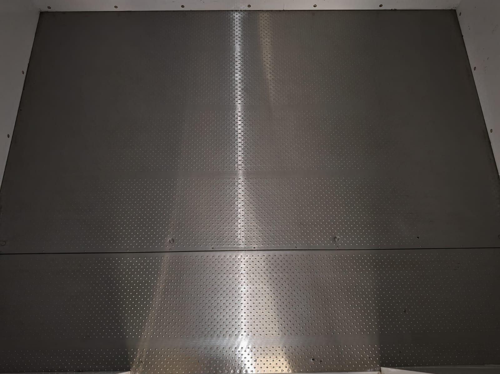 Metalowa podłoga w przestrzeni ładunkowej, z antypoślizgową fakturą i widocznymi łączeniami płyt, oświetlona centralnie, ukazująca czystość i gotowość do użytku.