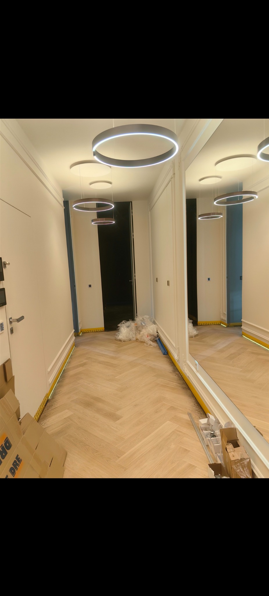 Jasne panele ułożone w jodełkę w korytarzu z lustrem i nowoczesnym oświetleniem. Kartony i folie zabezpieczające ściany sugerują świeżo zakończony montaż.