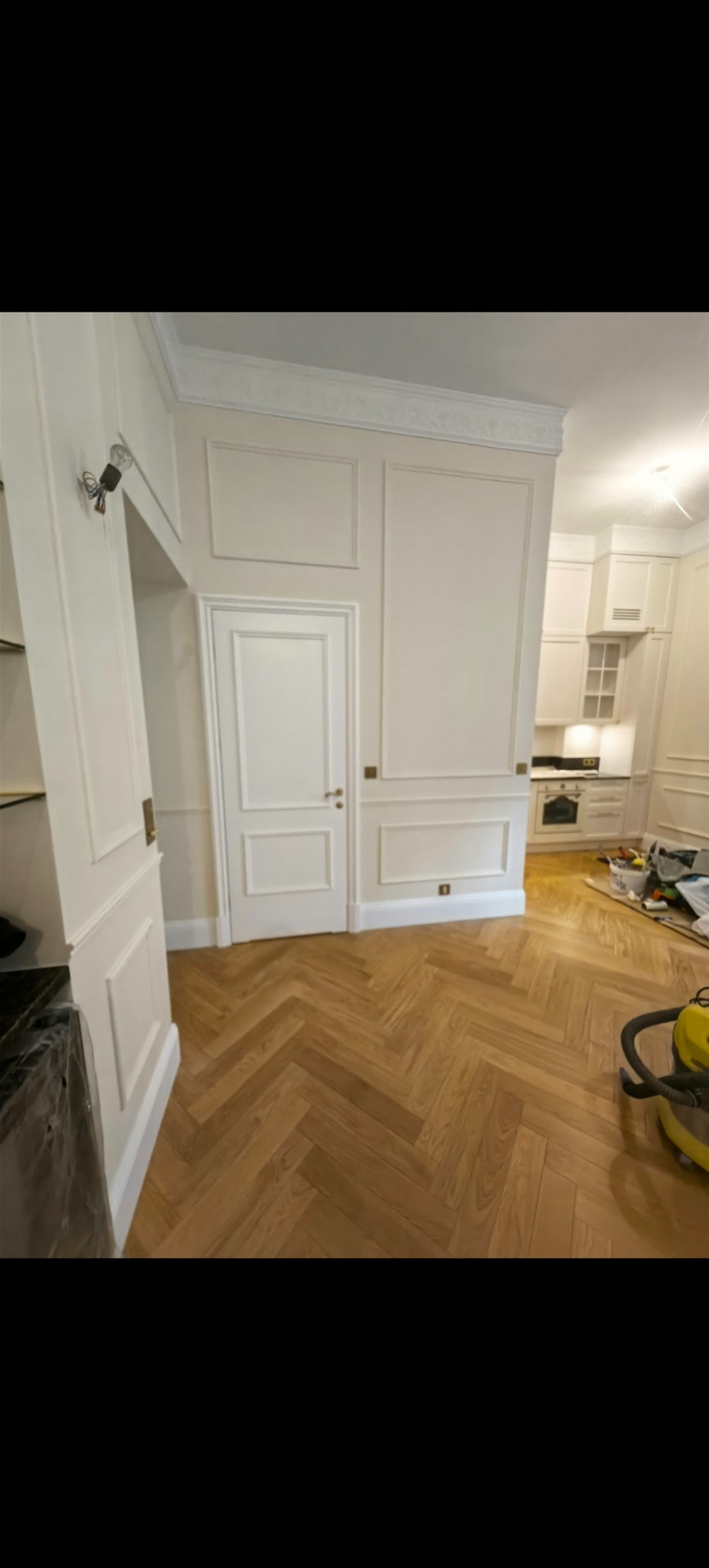 Eleganckie wnętrze po remoncie: parkiet w jodełkę, białe drzwi z frezowanymi panelami i listwami. Widoczny odkurzacz i narzędzia.