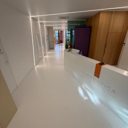 Grzegorz Fudalik - Biała posadzka żywiczna w nowoczesnym wnętrzu kliniki stomatologicznej Luxdentica, z oświetleniem liniowym i recepcją. Minimalistyczny design.