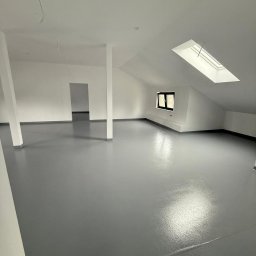 Grzegorz Fudalik - Szara, błyszcząca posadzka w jasnym, przestronnym pokoju na poddaszu z oknem dachowym i filarami. Minimalistyczne wnętrze po remoncie, świeżo wykończone.