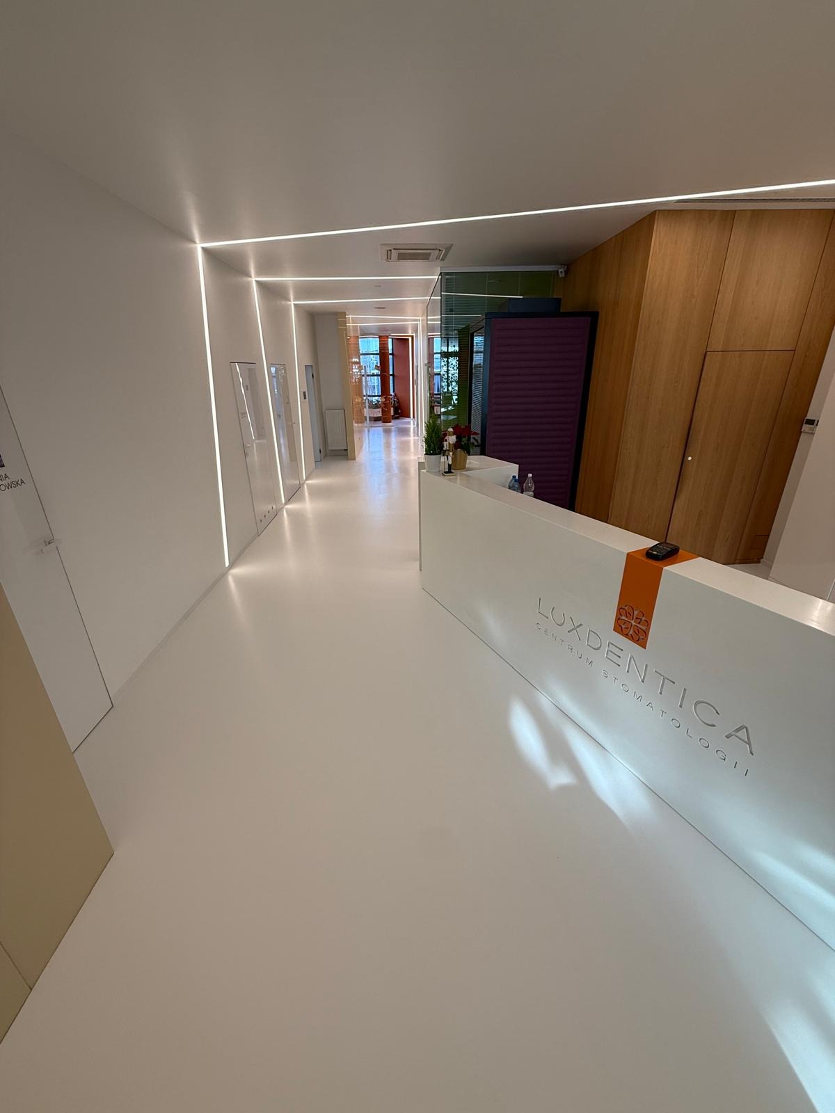 Biała posadzka żywiczna w nowoczesnym wnętrzu kliniki stomatologicznej Luxdentica, z oświetleniem liniowym i recepcją. Minimalistyczny design.
