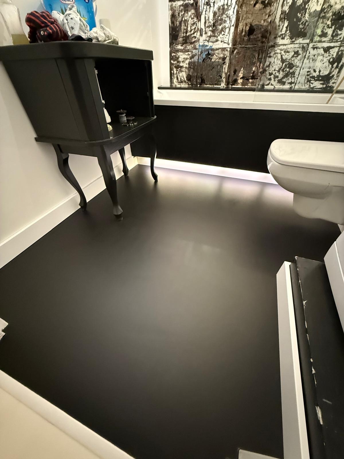 Czarne, błyszczące wykończenie posadzki żywicznej w łazience z toaletą i szafką na nóżkach. Nowoczesny design z oświetleniem LED przy wannie.