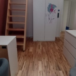 W-Grand Swietłana Makarewicz - Jasne drewniane schody prowadzą do antresoli w pokoju. Biała szafa z rysunkiem dziewczyny w słuchawkach. Parkiet z naturalnego drewna.