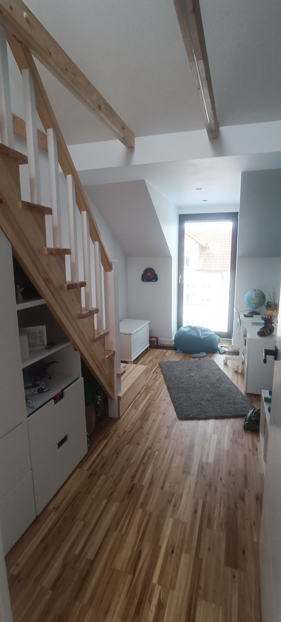 Jasne drewniane schody z białymi balustradami w nowoczesnym pokoju dziecięcym z drewnianą podłogą i elementami wystroju.